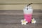 Cup of pink ice milk near Plumeria flowers on wooden floor.