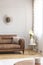 Cup on round wooden table in grey living room interior with blurred brown couch