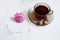 A cup and saucer of hot tea, a note and a flower on a white background. View from above