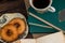 A cup of strong tea on a saucer, donuts on a plate and a stack of books on the table