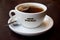 Cup of tea with Caffe Nero logo on white teacup with saucer and spoon on dark background.