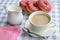 A cup of tea with cream, a creamer, a plate with pink donuts