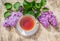 Cup of tea and fragrant lilac flowers. Summer lilac branch and tea in the garden.