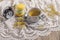 A cup of tea next to an alarm clock that strikes five o\\\'clock on a lace tablecloth with three stacked macarons