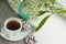 cup with tea on a saucer, chocolate chip cookies and a vase with bird cherry branches on a windowsill.