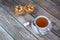 A cup of tea on a saucer with a spoon stands on a wooden table next to a napkin with two fresh muffins