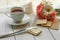 A cup of tea, several biscuits, a lace napkin and a bouquet of spring flowers on a white wooden surface