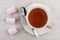 Cup of tea, spoon on saucer, pink marshmallows on table