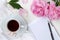 a cup of tea, a tablecloth, flowers peonies, petals and leaf on a white table.