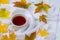 Cup of tea, warm white scarf and scattered autumn leaves on a white wooden table. Autumn concept