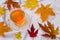 Cup of tea, warm white scarf and scattered autumn leaves on a white wooden table. Autumn concept