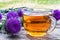 A cup of thistle tea on a woody background on nature. Thistle flowers near the cup with tea.