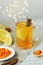 Cup of vitamin anti-cold tea with lemon slices, sea buckthorn berries and cinnamon with festive garland on wall and ingredients on