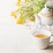 Cup of yellow herbal tea on white table background with teapot and fresh healing herbs and flowers. Herbal medicine. Natural