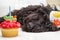 Cupcake with candle in the foreground and black furry dog lying on white chair wearing a birthday party hat in the background