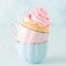 Cupcake with gentle pink cream decoration in two cups on blue pastel background.