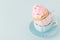 Cupcake with gentle pink cream decoration in two cups on blue pastel background.