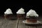 Cupcake topped with whipped cream on a small ceramic saucer. Two more cupcakes are in a blurry background.