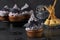 Cupcakes with colorful cream decorated with mastic bats and witch's brooms made of cheese and straw for Halloween party