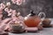 Cups of brewed tea, teapot and sakura flowers on grey table. Generative AI