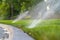 Curb of the paved road with water sprinklers on the vivid green grassy roadside