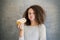 Cure curly hair girl eating croissant against wall