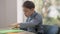 Curios autistic Caucasian boy sitting at table with colorful paper smiling looking away. Portrait of cute child with