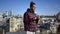 Curios talented African American young man taking photos of downtown on camera standing on rooftop. Portrait of absorbed