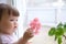 Curiosity childness. curious baby girl portrit in pink clothes one year old on the window with geranium flower