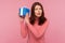 Curious brunette woman in pink sweater shaking blue giftbox near ear trying to guess her present