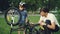 Curious child wearing helmet is spinning bicycle wheel and pedals while his father is talking to him on lawn in park on