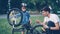 Curious child wearing helmet is spinning bicycle wheel and pedals while his father is talking to him on lawn in park on