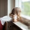 Curious cute little girl standing on a chair at the window, blonde curls