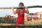 Curious farm girl wearing polka dot kids pans looking at field with working red combine harvesters