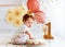 Curious funny baby boy poking finger in his first birthday cake