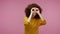 Curious girl afro hairstyle in hoodie looking through hands binocular gesture, zooming observing distance