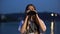 Curious girl spending evening on river embankment, looking through binoculars