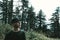 Curious hiker looking up at sky in front of pine trees