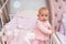 Curious infant baby in pink crib and bedroom scene.