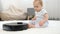 Curious little baby boy looking at robot vacuum cleaner riding on carpet at living room