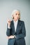 Curious senior businesswoman with arm up on grey