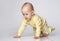 Curious Toddler infant kid crawling on a gray studio background, he dressed with yellow children's cotton overalls with