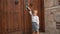 Curious toddler stands near big wooden door moving handle