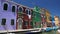 Curious tourists walking street on Burano island, photographing colored houses