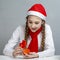 Curious Winsome Caucasian Female Girl in Santa Hat and White Shirt Holding Tiny Red Gift Box While Looking Inside With Excited