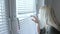 Curious young woman spying, peeking through the blinds in her home