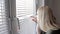 Curious young woman spying, peeking through the blinds in her home