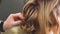 A curl on the head of a girl with brown hair is corrected by a hairdresser, sprays with varnish and combs with a comb on