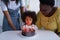 curly african american girl blowing out candles on birthday cake near granny and mom,stock image