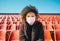 Curly girl in a surgical mask sitting in an empty stadium during epidemic disease Covid-19